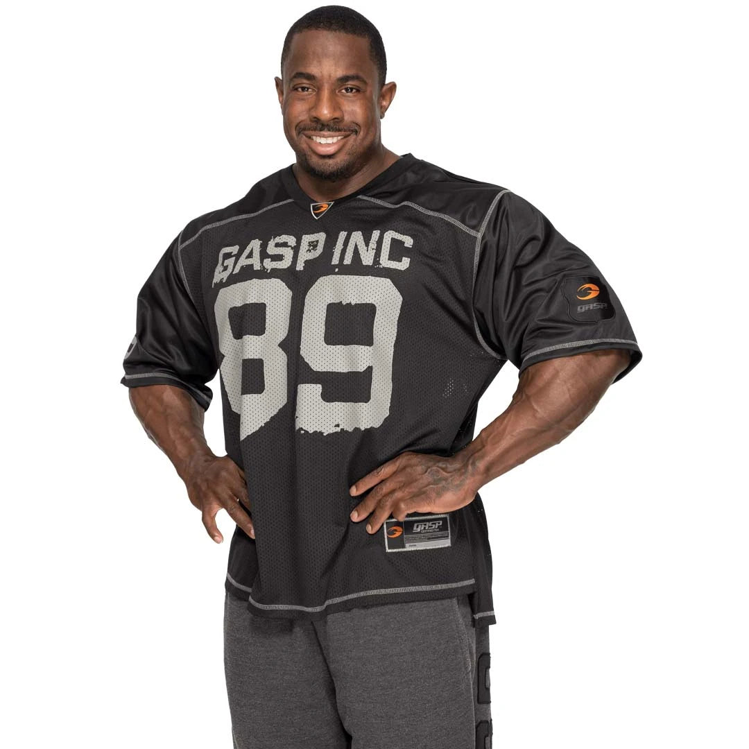 Musta oversize-mallinen GASP No1 Football Tee Black -mesh-paita harmaalla painatuksella miehen yllä.