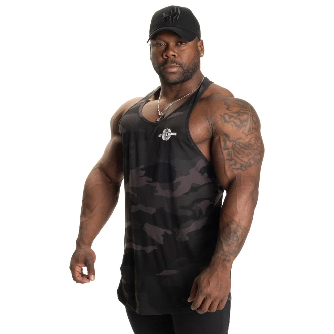 Better Bodies Essential T-back V2 Dark Camo är ett mörkt kamouflerat träningslinne i bomull som bärs av en man., bild 3 av 6