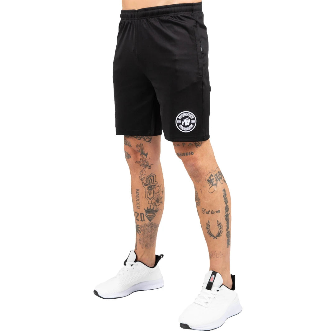 Gorilla Wear Vernon Track Shorts Black -mustat treenishortsit valkoisella logolla tatuoidun mallin yllä.