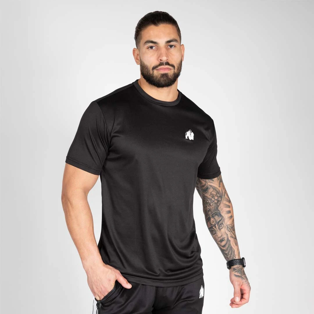 Gorilla Wear Fargo T-Shirt Black, musta treenipaita ilmavaa polyesteriä valkoisella logolla, mallin yllä.