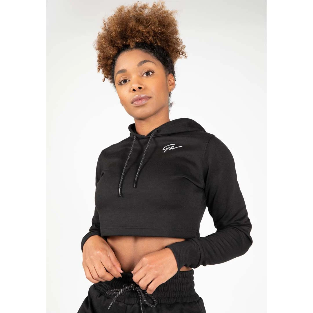 Kvinna i Gorilla Wear Pixley Crop Top Hoodie Black, en svart croppad huvtröja med vit logga och dragsnöre., bild 5 av 5