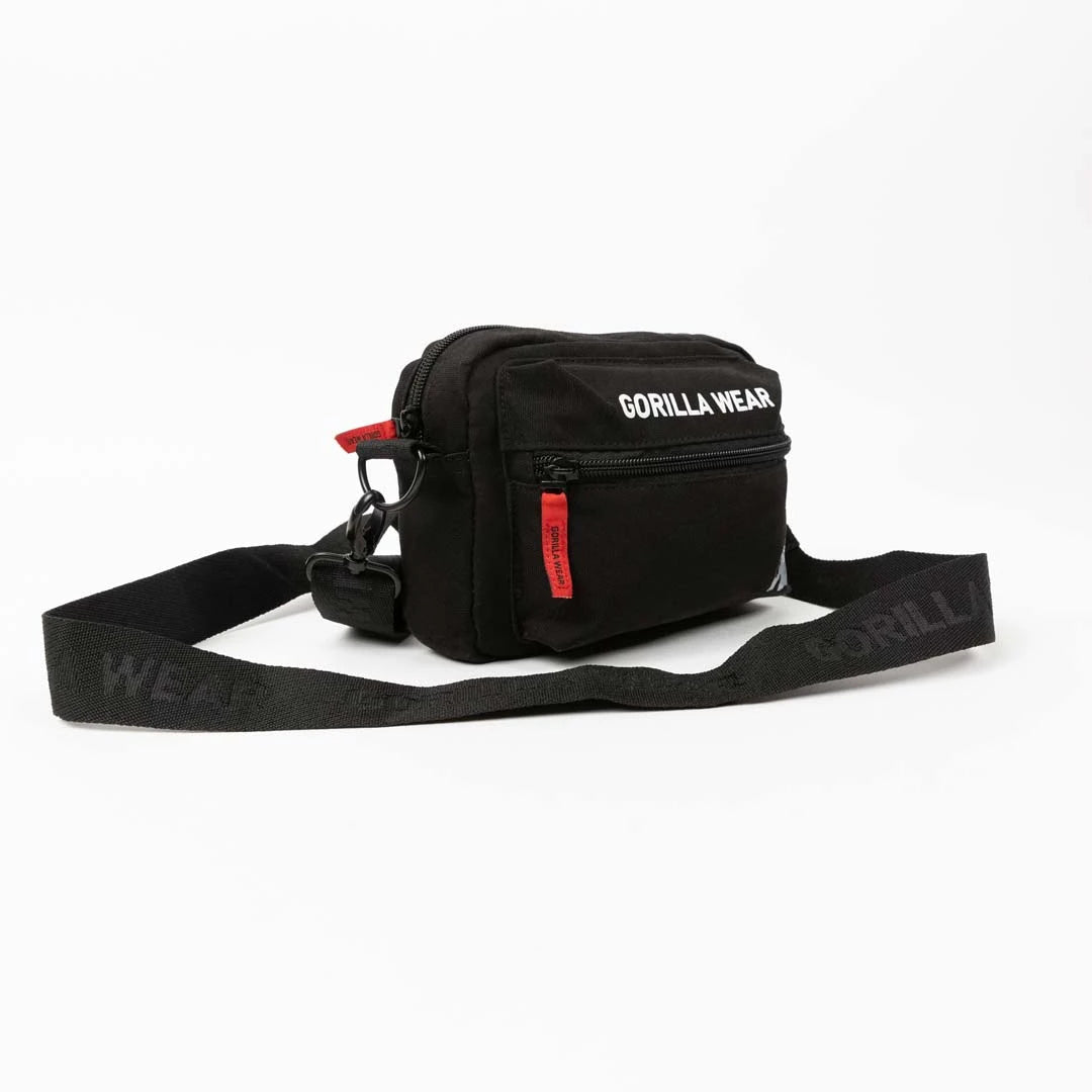 Gorilla Wear Brighton Crossbody Bag Black mustasta puuvillasta hihnalla, valkoisella logolla ja punaisilla vetoketjuilla.